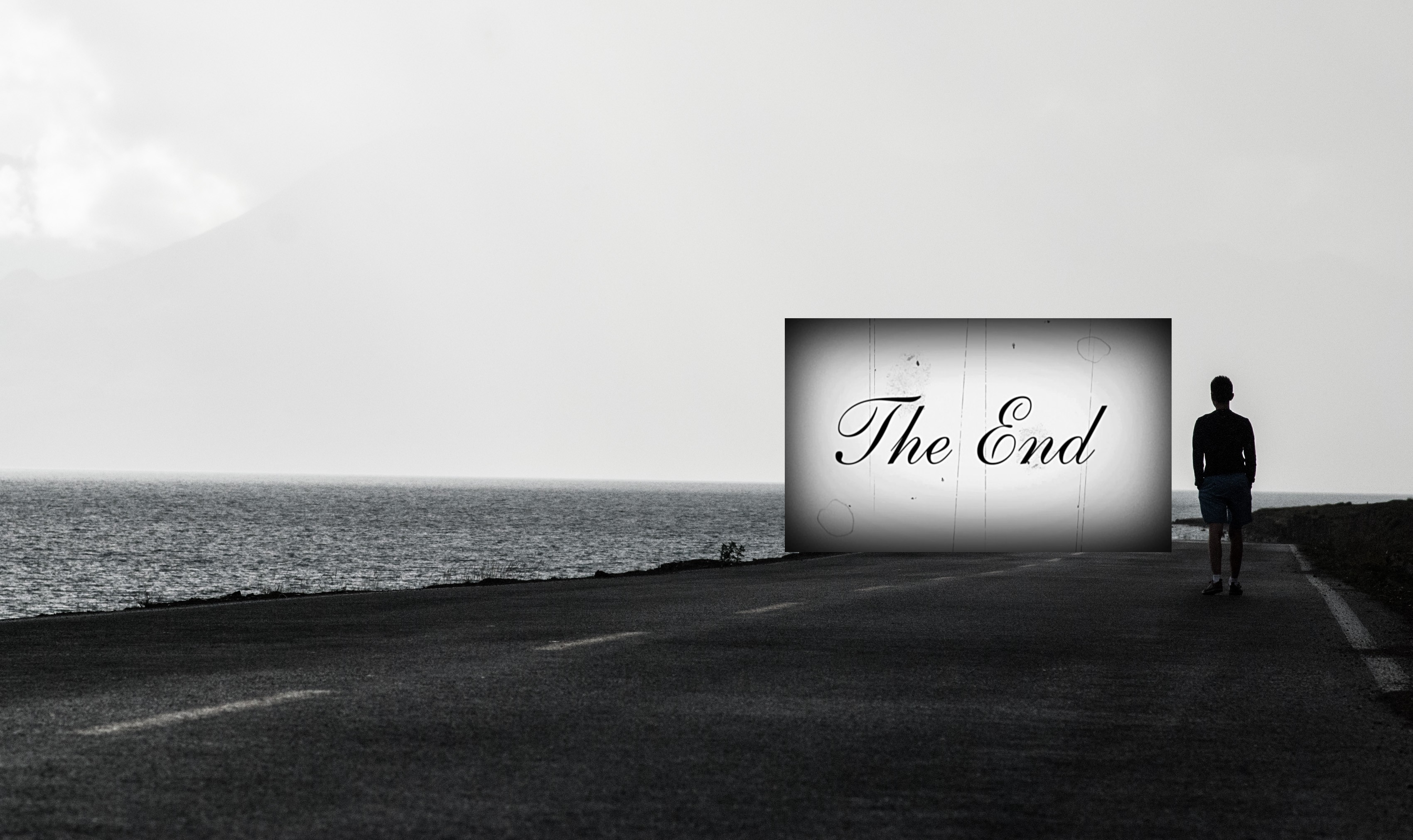 A black and white photo of a person in running clothes standing on a road beside the ocean with a big, digital screen that reads "The End" in front of the person