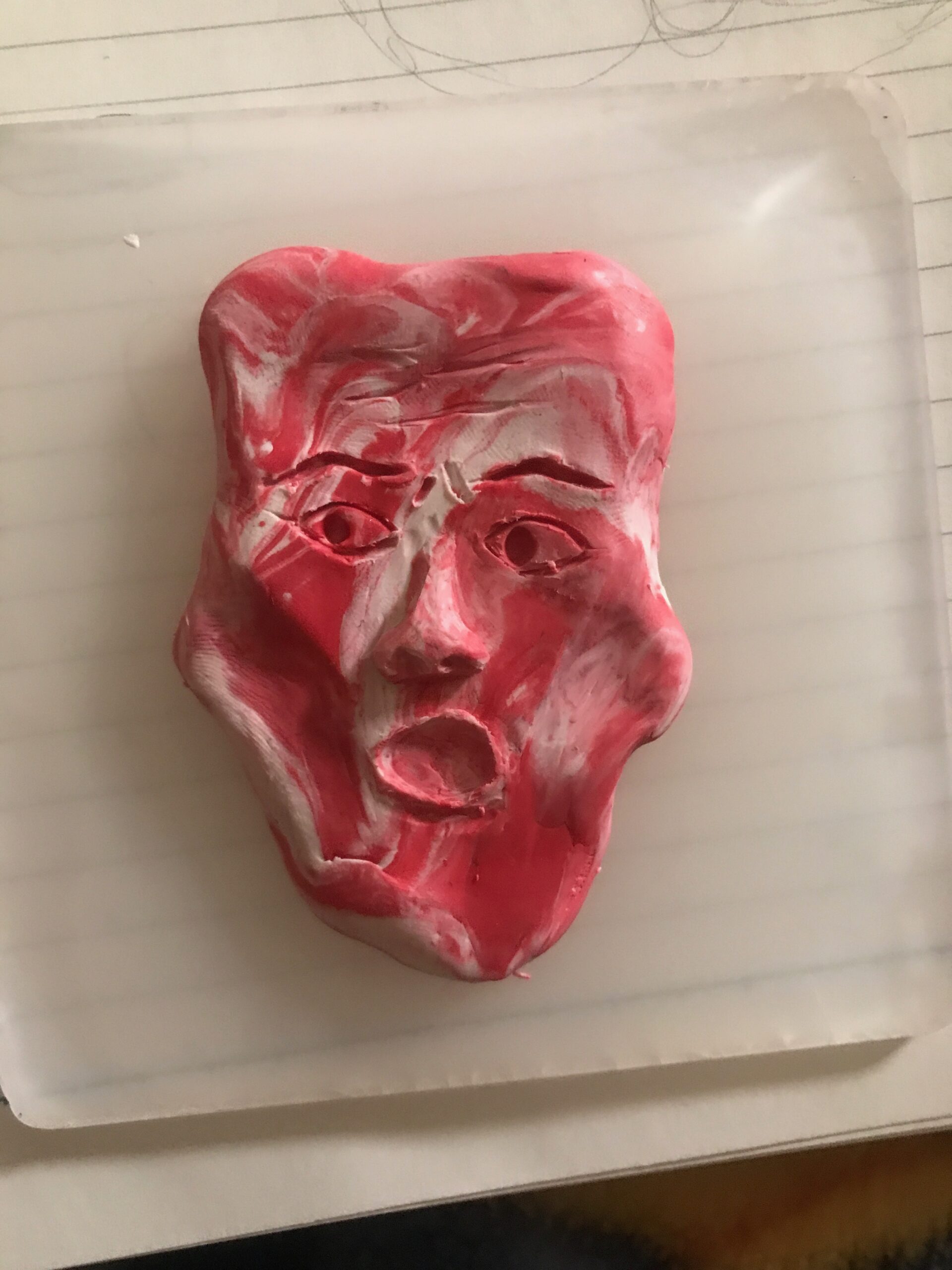 A red and white marbled clay face with high cheekbones, a flat and square top of the head, and a wide open mouth like they are shocked